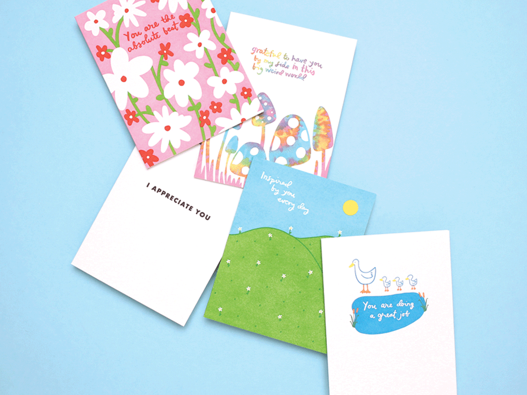 cards scattered on top of one another featuring flowers, mushrooms, floral hillsides, a duck family and white background one that says i appreciate you